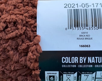 Puede incluir: Un ovillo de hilo super grueso de color rojo ladrillo. El hilo está etiquetado como "Color by Nature" y tiene el número de colección 166063. El hilo mide 10 cm x 10 cm y tiene un grosor de 8 mm.