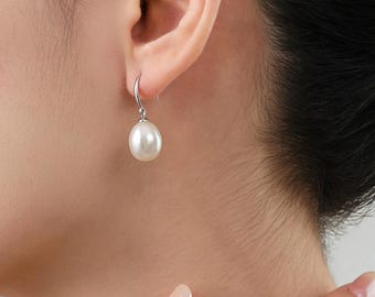 May include: A single pearl earring with a silver hook is shown. The white pearl hangs below the ear. The earring is a classic design, suitable for everyday wear or special occasions. The earring is shown on a person.
