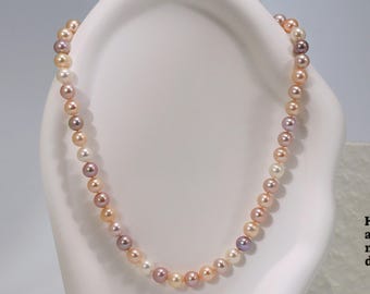 May include: A necklace featuring a strand of round, lustrous pearls in varying shades of white, cream, peach, and soft lavender. The pearls are arranged in a repeating color pattern. Next to the necklace is a card with the text Have a nice day.