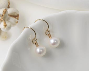 May include: A pair of gold-colored drop earrings with white, round pearls. The earrings are displayed on a white, curved surface. The text "PearlFans" is visible at the bottom of the image.