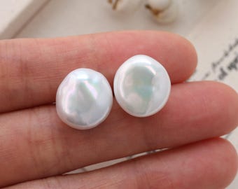 May include: Two iridescent white pearl earrings with a flat, round shape. The pearls have a smooth, lustrous surface and are set against a soft background. The earrings are a classic jewelry item.