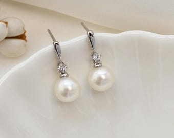 May include: A pair of elegant drop earrings featuring lustrous white pearls. The earrings have a silver-colored metal design with a small, sparkling accent above each pearl. The brand name "PearlFans" is printed in black at the bottom.