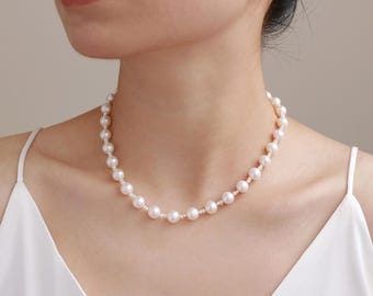 May include: A delicate pearl necklace with a strand of round, white pearls. The necklace is worn around the neck, and the pearls are evenly spaced. The background is a neutral color, highlighting the necklace.