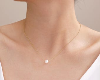 May include: A delicate gold necklace featuring a single, luminous white pearl pendant. The fine chain drapes gracefully, showcasing the pearl's subtle luster. The necklace is a simple yet elegant piece of jewelry.