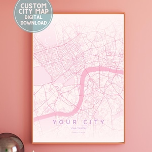 May include: A framed custom city map in shades of pink, with the text "YOUR CITY" and "YOUR COUNTRY" at the bottom. The map is a digital download, as indicated by the circular text overlay. The artwork is displayed on a pink wall.