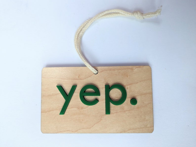 Puede incluir: Un letrero de madera con una cuerda blanca atada en la parte superior. El letrero tiene la palabra "yep" escrita en letras verdes.