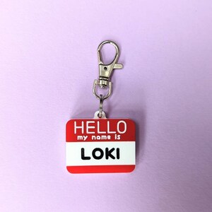 May include: Red plastic name tag with a silver clip. The tag says "HELLO my name is LOKI".