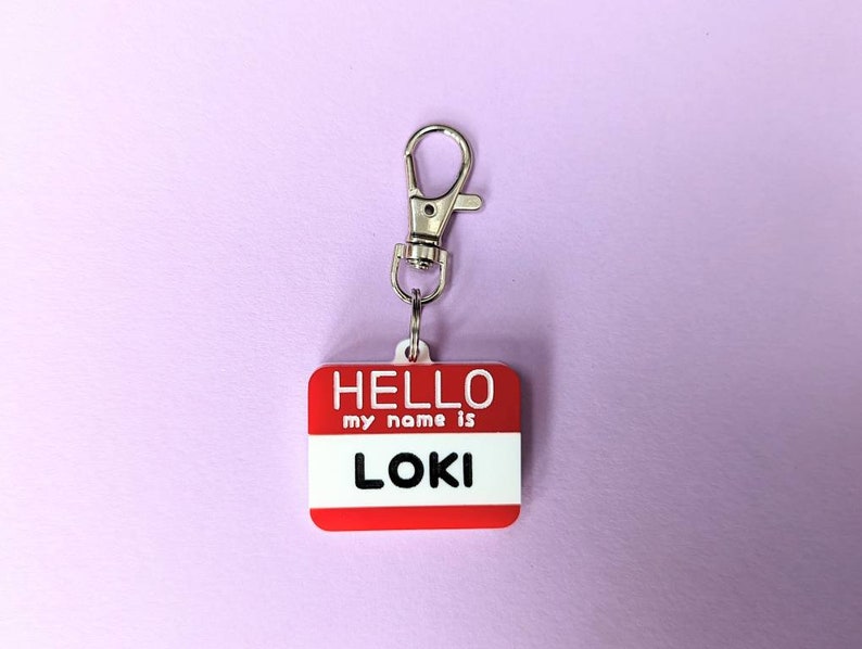 May include: Red plastic name tag with a silver clip. The tag says "HELLO my name is LOKI".