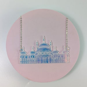May include: A silver chain necklace with a clear iridescent pendant featuring a detailed silhouette of a building with multiple domes and towers.