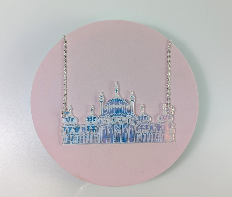 May include: A silver chain necklace with a clear iridescent pendant featuring a detailed silhouette of a building with multiple domes and towers.