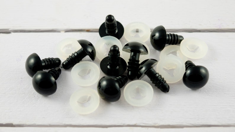 May include: A close-up of black plastic safety eyes with white plastic washers. The eyes are about 1 inch in diameter and have a screw-on back.