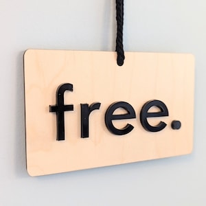 Puede incluir: Un letrero de madera con la palabra "free" en letras negras. El letrero está colgado de una cuerda negra.