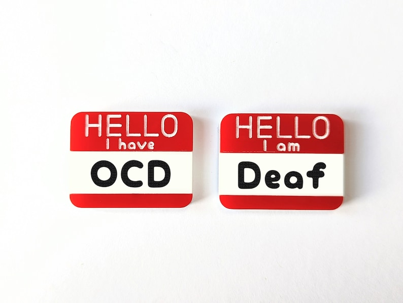 May include: Two red name tags with white text. The first tag says "Hello I have OCD". The second tag says "Hello I am Deaf".