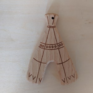 May include: A wooden teepee ornament with a brown stain and engraved details. The teepee has a small hole at the top for hanging.