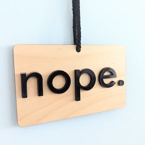 May include: A wooden sign with the word "nope" in black letters. The sign is hanging from a black string.