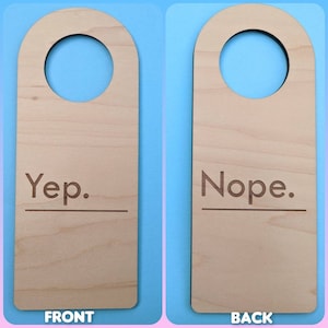 Puede incluir: Colgador de puerta de madera con un agujero redondo en la parte superior. El lado delantero dice "Yep." y el lado trasero dice "Nope."