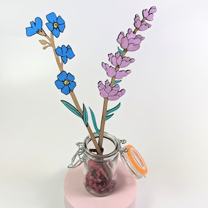May include: Two wooden flower stems in a glass jar with a lid. The flowers are painted blue and purple. The jar is filled with red and brown paper shreds.