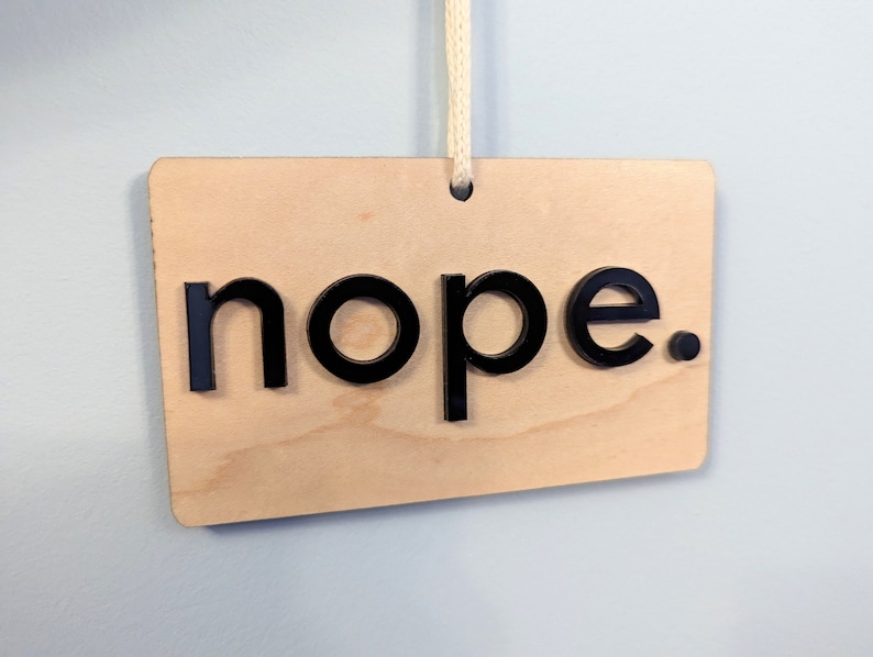 Puede incluir: Un letrero de madera con la palabra "nope" en letras negras.