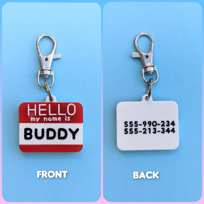 May include: Red and white plastic name tag with the text "HELLO my name is BUDDY" on the front and phone numbers "555-990-234 555-213-344" on the back. The tag is attached to a silver key ring.
