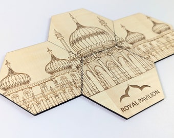 May include: A set of six hexagonal wooden coasters featuring a laser-etched design of the Royal Pavilion in Brighton, England. The coasters are made of light-coloured wood and have a black border. The design includes intricate details of the building's architecture, including the domes, windows, and arches. The coasters are arranged in a circular pattern, with the text "ROYAL PAVILION" printed on one of the coasters.