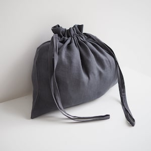 Peut inclure: Un sac en lin gris foncé avec des cordons de serrage. Le sac est fait d'un tissu doux et naturel et a un design simple et élégant.