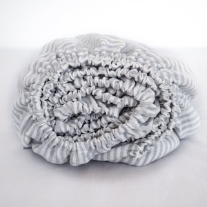 Könnte beinhalten: Ein zusammengerolltes, grau-weiß gestreiftes Spannbettlaken.