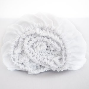 Peut inclure: Un drap-housse blanc roulé, avec des bords élastiques. Le drap est fait d'un tissu doux et léger, conçu pour s'adapter à un matelas. Les bords élastiques sont froncés, créant un aspect froissé. Le drap est de couleur blanche unie.