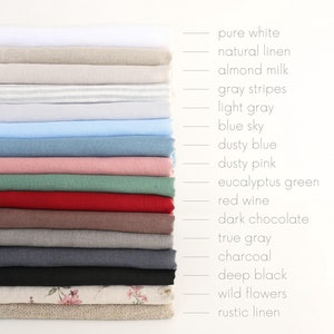 Pode incluir: Uma pilha de 16 tecidos de linho de diferentes cores, incluindo branco puro, linho natural, leite de amêndoa, listras cinzas, cinza claro, céu azul, azul poeira, rosa poeira, verde eucalipto, vinho tinto, chocolate escuro, cinza verdadeiro, carvão vegetal, preto profundo, flores silvestres e linho rústico.