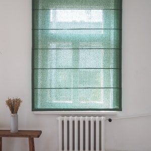K&ouml;nnte beinhalten: Ein gr&uuml;ner Leinen-Rollladen h&auml;ngt an einem Fenster mit einem wei&szlig;en Heizk&ouml;rper darunter.