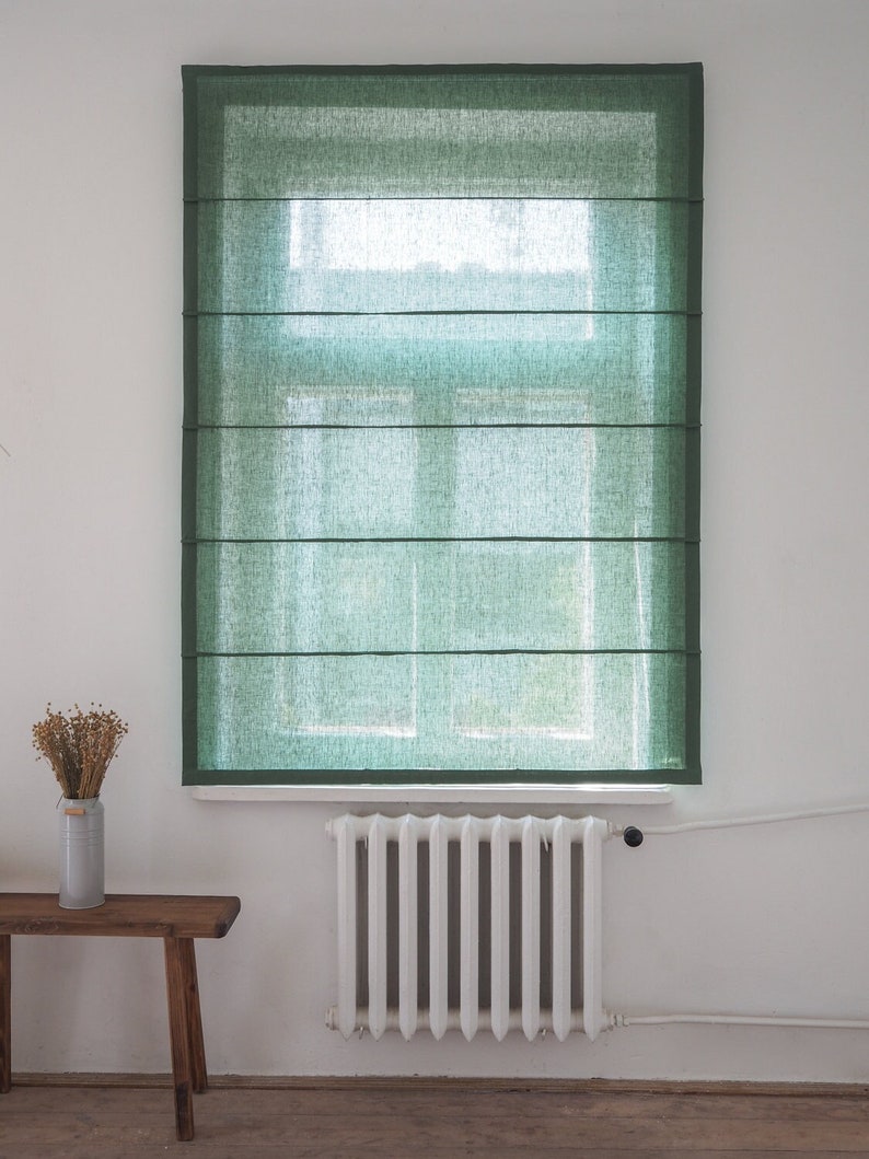 K&ouml;nnte beinhalten: Ein gr&uuml;ner Leinen-Rollladen h&auml;ngt an einem Fenster mit einem wei&szlig;en Heizk&ouml;rper darunter.