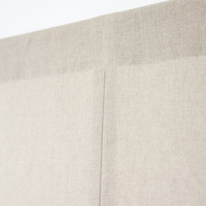 May include: Close-up of a beige fabric headboard with a seam down the centre.
