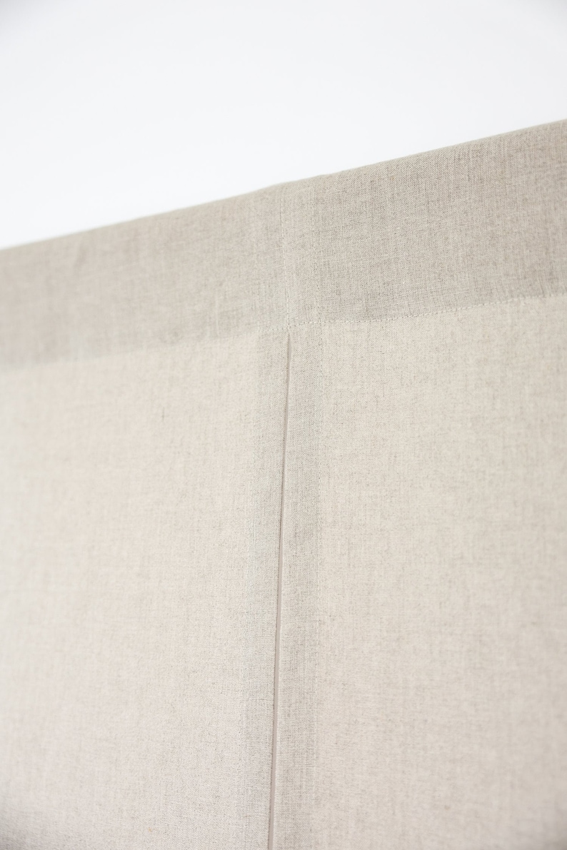 May include: Close-up of a beige fabric headboard with a seam down the centre.
