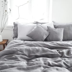 May include: A gray linen duvet cover with a white pillow and gray throw pillows on a bed. The bed is in a bedroom with a window in the background.