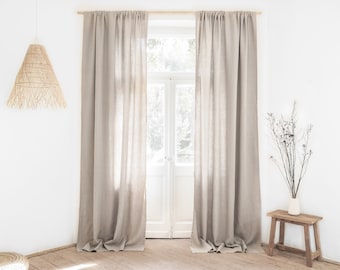 Könnte beinhalten: Zwei hellbeige Leinenvorhänge hängen an einem Fenster, mit einer Holzstange oben. Die Vorhänge sind an den Seiten zusammengezogen, und der Stoff ist leicht zerknittert. Das Fenster ist geöffnet, und im Hintergrund sind Bäume und ein Haus zu sehen.