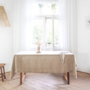 May include: A light brown linen tablecloth draped over a wooden table with a woven basket and a wooden stool in the background.