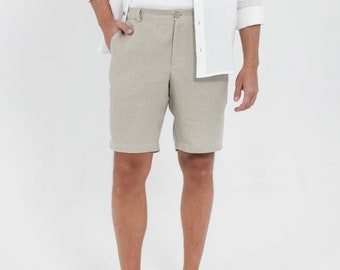 Op de afbeelding: Een beige linnen broek met een knoopsluiting en riemlussen. De broek wordt gedragen door iemand die een wit linnen overhemd draagt.