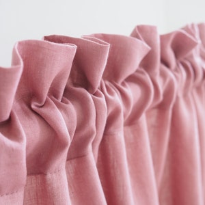 Könnte beinhalten: Ein Satz rosa Rüschenvorhänge aus weichem, strukturiertem Stoff. Die Vorhänge sind oben gerafft und hängen in weichen Falten.