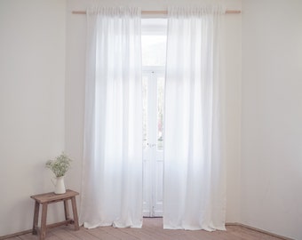 Puede incluir: Dos cortinas de lino blanco cuelgan de una barra de madera delante de una ventana. Las cortinas son transparentes y permiten que la luz se filtre. La ventana está cerrada y las cortinas están tiradas a los lados.