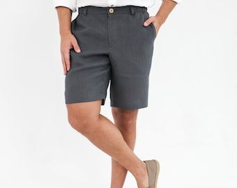 Op de afbeelding: Een man draagt een wit overhemd met knopen en een donkergrijze linnen broek. Hij draagt ​​bruine canvas slip-ons.