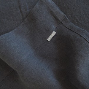 Op de afbeelding: Een donkergrijze linnen stof met een klein wit label met de tekst "so linen!"