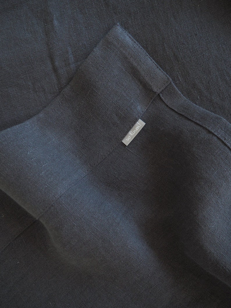 Op de afbeelding: Een donkergrijze linnen stof met een klein wit label met de tekst "so linen!"