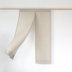 May include: A beige linen scarf with a fringed edge hangs from a wooden rod against a white wall.