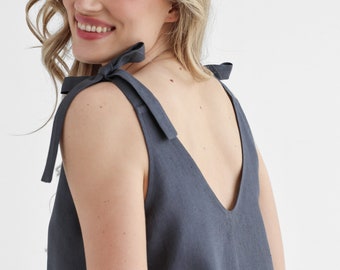 Puede incluir: Un vestido de lino gris oscuro sin mangas con escote en V y tirantes de lazo. El vestido es holgado y tiene un estilo informal y relajado.
