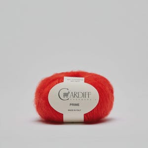 以下が含まれることがあります： 鮮やかな赤色の毛糸玉。ラベルには「Cardiff Cashmere Prime」と記載されています。ラベルには、この糸がカシミア68％、シルク32％であることも記載されています。イタリア製です。