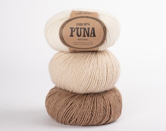 Puede incluir: Tres ovillos de lana apilados uno encima del otro. El ovillo superior es blanco con una etiqueta marrón que dice "DROPS PUNA NATURAL". El ovillo del medio es de color beige claro y el ovillo inferior es de color marrón claro.