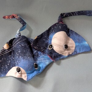 May include: Two plush toys shaped like manta rays. The toys feature a dark blue fabric with a galaxy print, white accents, and light tan faces with black button eyes. The wings are curved and the tails are long and curved.