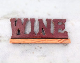 May include: A wooden sign with the word "WINE" painted in red on a white background. The sign is mounted on a wooden base.