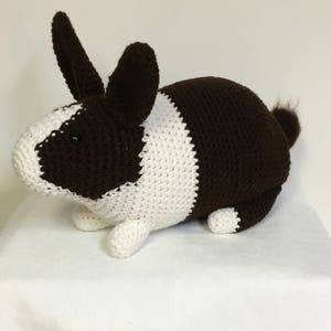 May include: A crocheted stuffed rabbit toy with brown and white fur. The rabbit has long ears and a small tail.