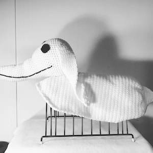May include: A white crocheted ghost character with black eyes and a stitched smile. The ghost is sitting on a black metal rack.