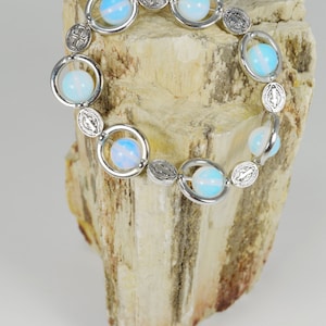 May include: A silver bracelet with blue and white opal beads and silver charms. The bracelet is on a piece of petrified wood.